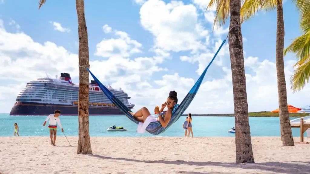 Guest relaxing in a beach hammock with a Disney cruise ship offshore