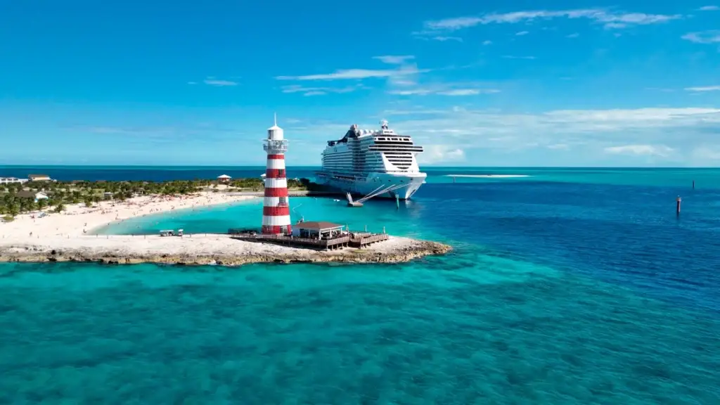 Cruise ship anchored off a private island beach with a lighthouse