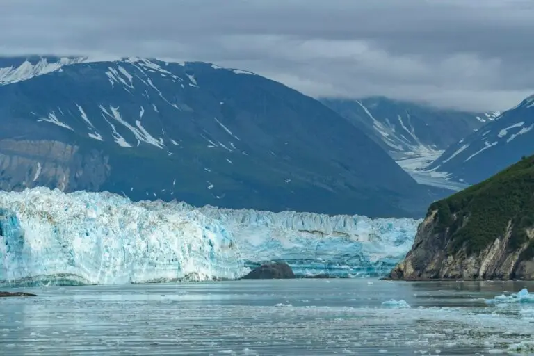 Tidewater glacier meeting the sea beneath snowy peaks in Alaska